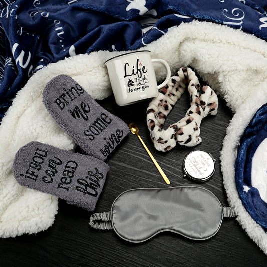 Set of sleep accessories including eye mask, slippers, mug, and blanket on a dark surface.