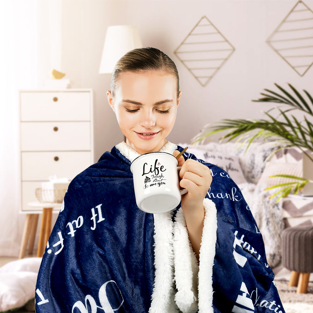 Woman holding a mug wrapped in a blue blanket with white text in a cozy room.