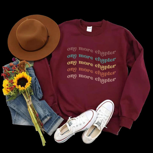 Maroon sweatshirt with 'one more chapter' text, white sneakers, brown hat, jeans, and sunflowers on a wooden surface.