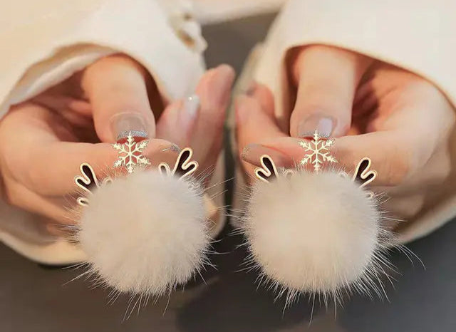 Close-up of hands wearing white fluffy earrings with snowflake decorations.