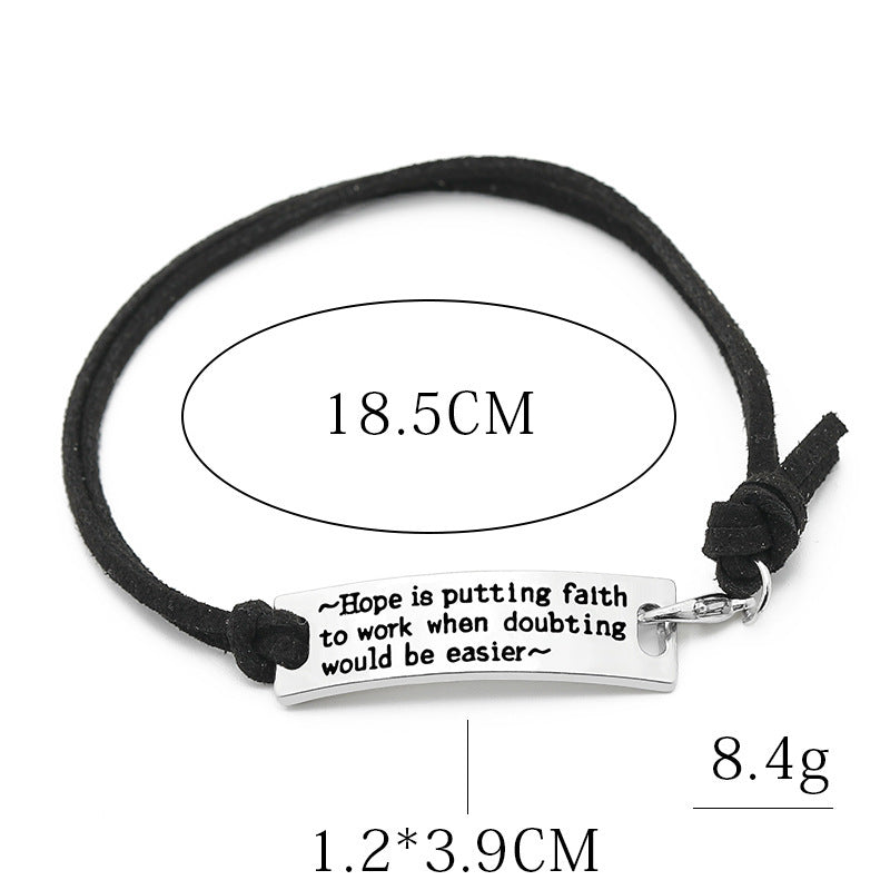 Black cord bracelet with a silver tag featuring an inspirational quote, shown on a white background.