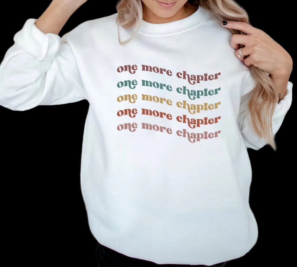 White sweatshirt with 'one more chapter' text in multiple colors worn by a person.