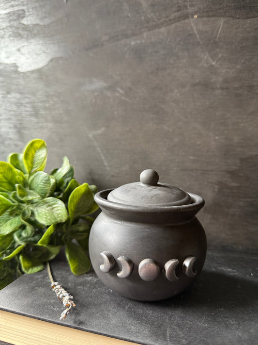 Ceramic jar with moon phase design on a dark surface with a plant in the background