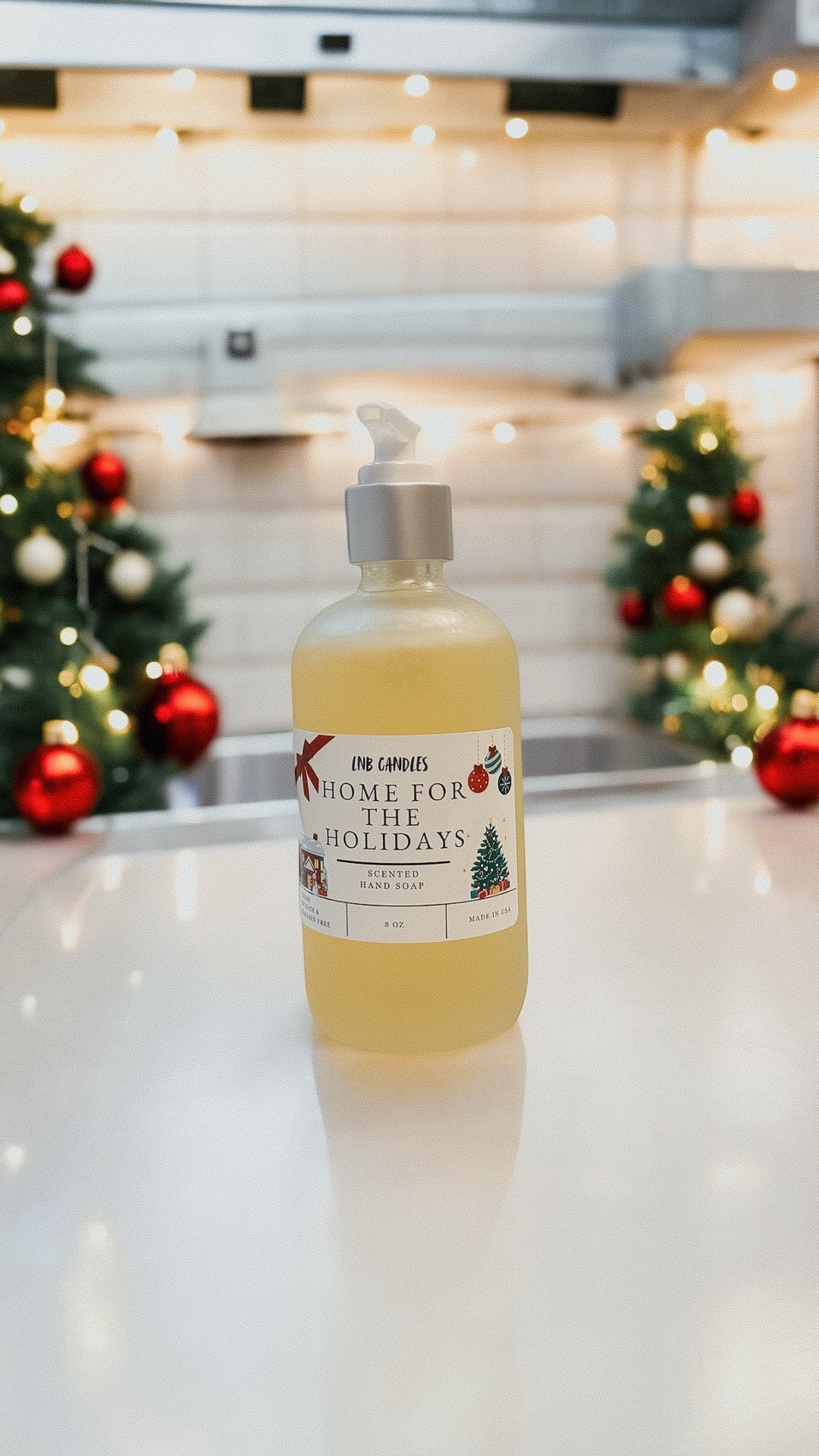 Bottle of soap with a Christmas-themed label on a kitchen counter with decorated trees in the background.
