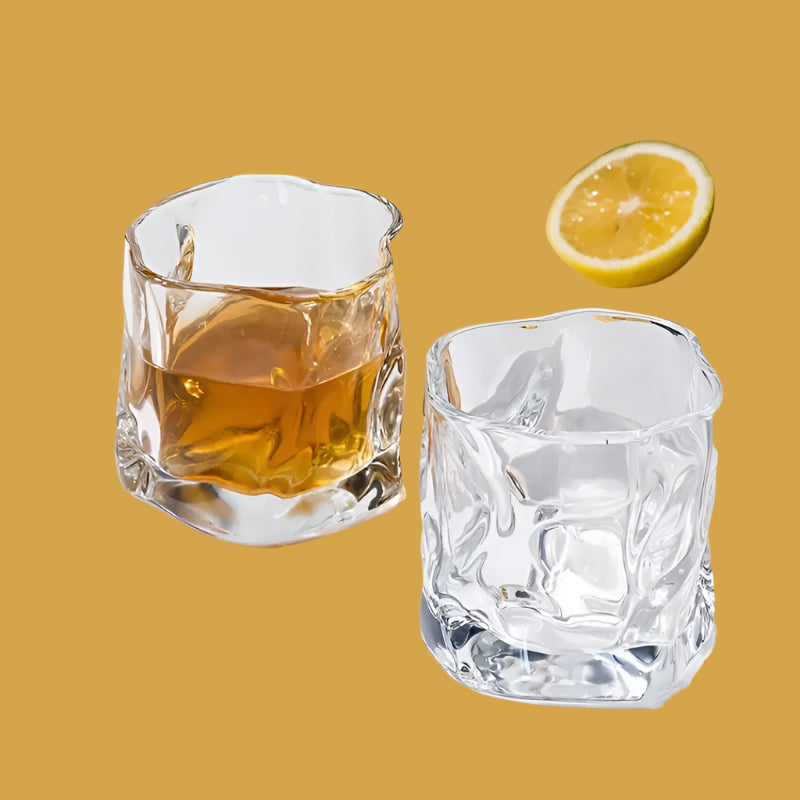 Two clear glasses with one containing a yellow liquid and the other empty, on a white surface with a lemon half.
