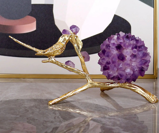 Decorative piece with gold bird and purple spherical object on a reflective surface