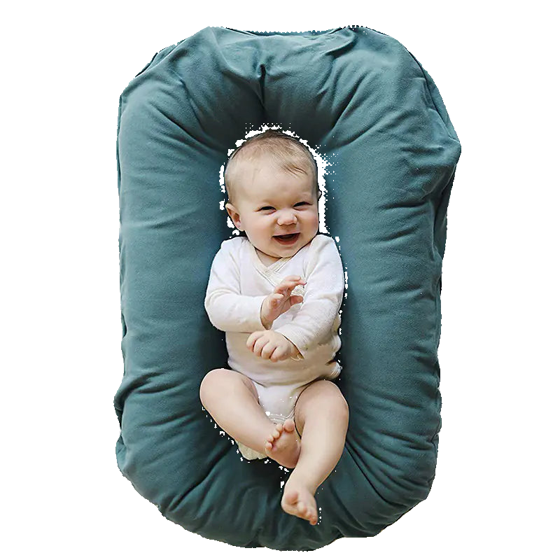 Baby lying on a green U-shaped pillow against a white background