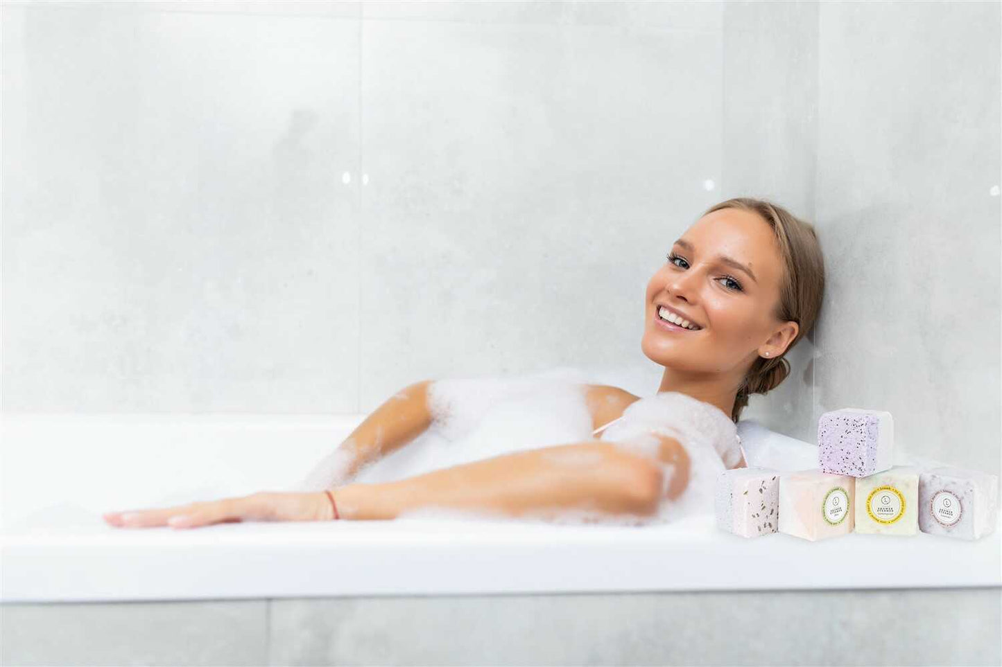 Woman relaxing in a bubble bath with bath bombs on a white background