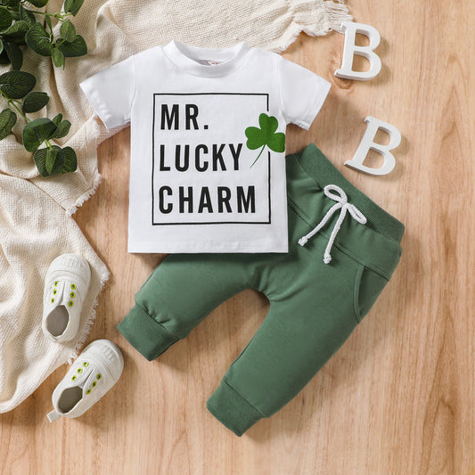Children's outfit with 'MR. LUCKY CHARM' shirt, green pants, and white shoes on a wooden surface.