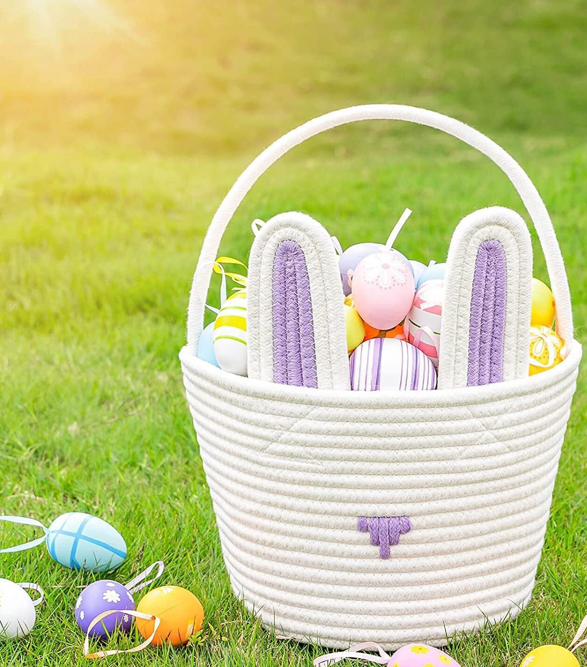 White woven Easter basket with bunny ears filled with colorful eggs on a grassy background