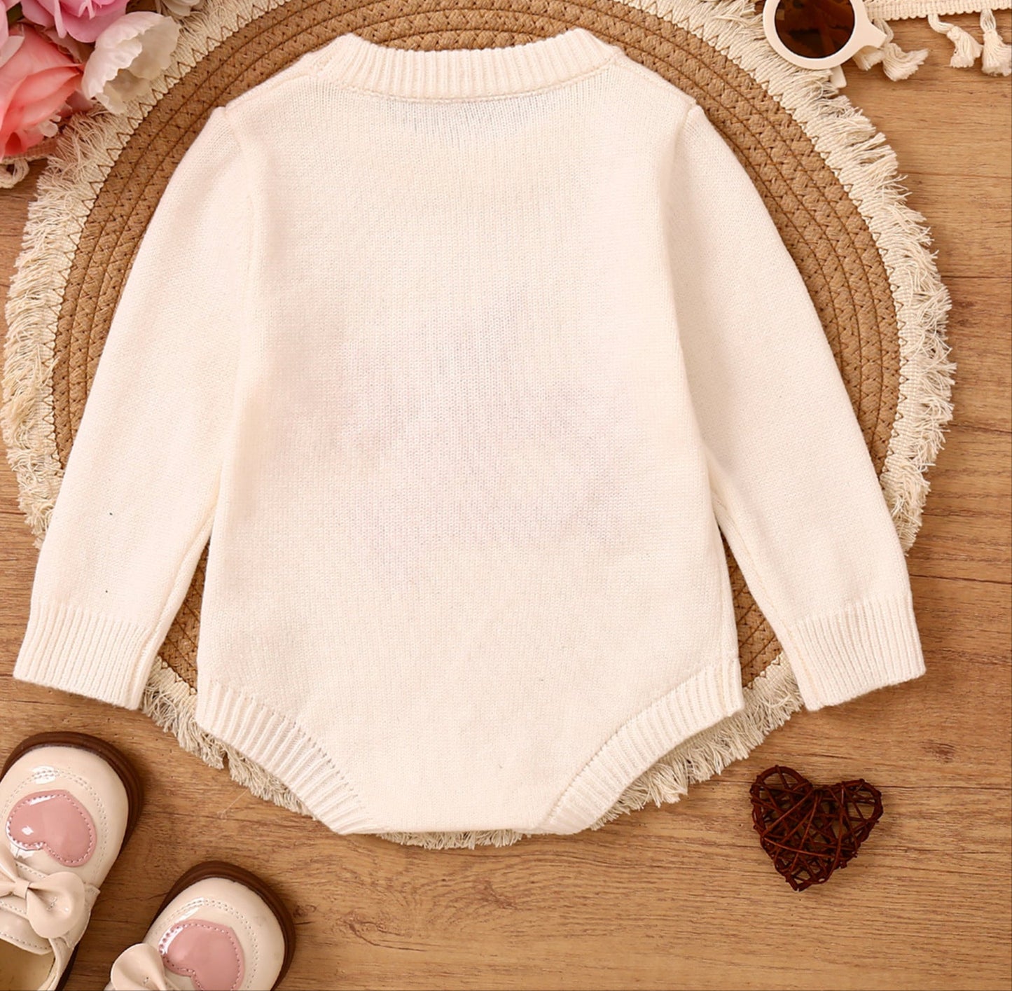 White sweater on a wooden surface with flowers, sunglasses, and shoes around it.
