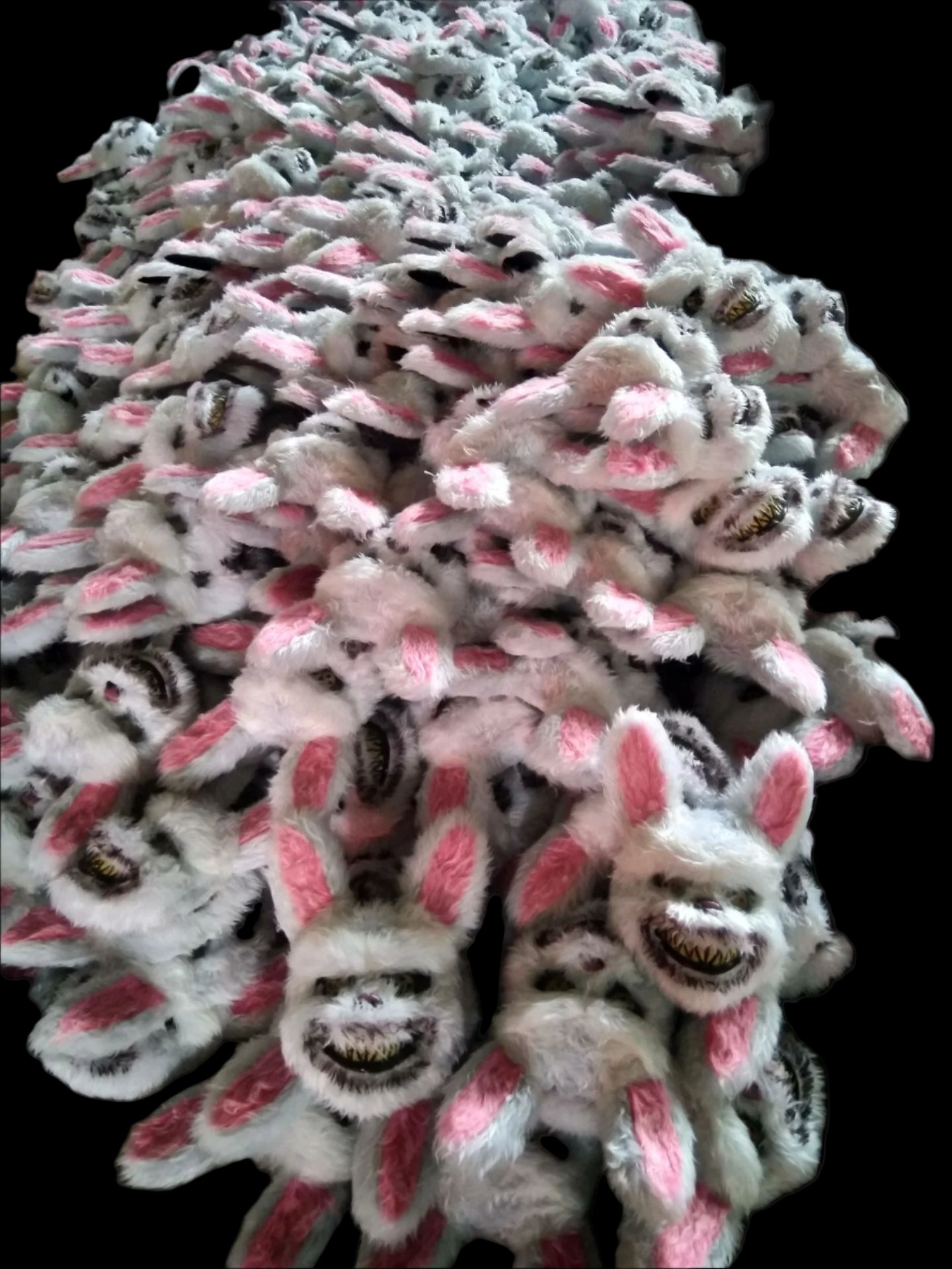 Stack of plush bunny slippers with black eyes and pink ears.