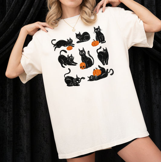 Person wearing a white t-shirt with black cat and pumpkin designs on a plain background