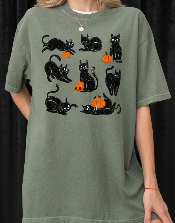 Person wearing a green t-shirt with black cat and orange pumpkin designs on a plain background