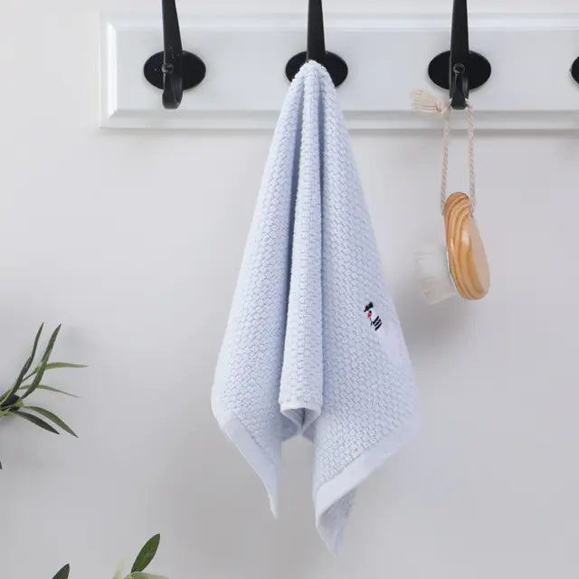 Light blue towel hanging on a black hook against a white wall with a plant in the corner.