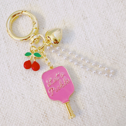 Keychain with pink pickleball paddle and cherry charm on a textured white background