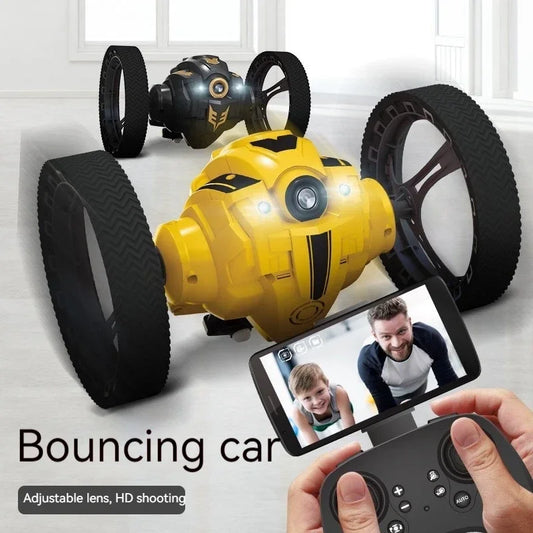 Yellow bouncing car with black wheels and a smartphone displaying a video call, on a light gray surface.