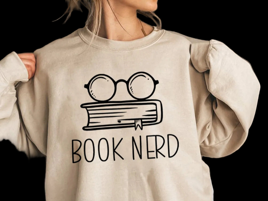 Person wearing a beige sweatshirt with 'Book Nerd' design and glasses on a book.