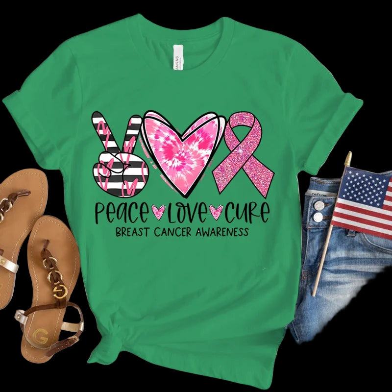 Green t-shirt with breast cancer awareness design featuring a peace sign, heart, and pink ribbon on a wooden surface.