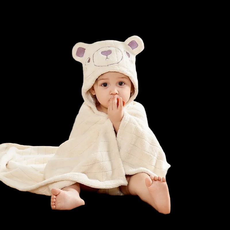 Child wrapped in a white hooded towel with bear ears, sitting on a bed with Aibedila logo.