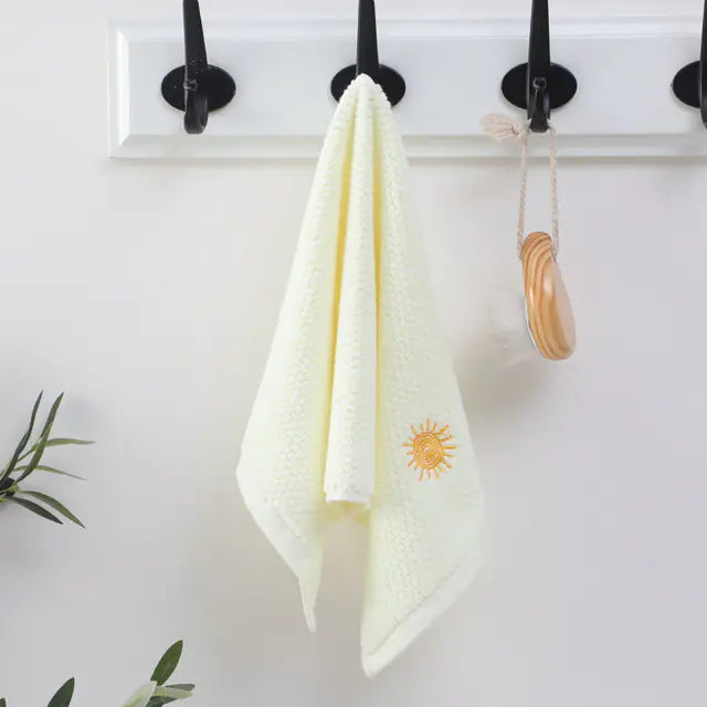 White towel with a sun emblem hanging on a wall with black hooks.