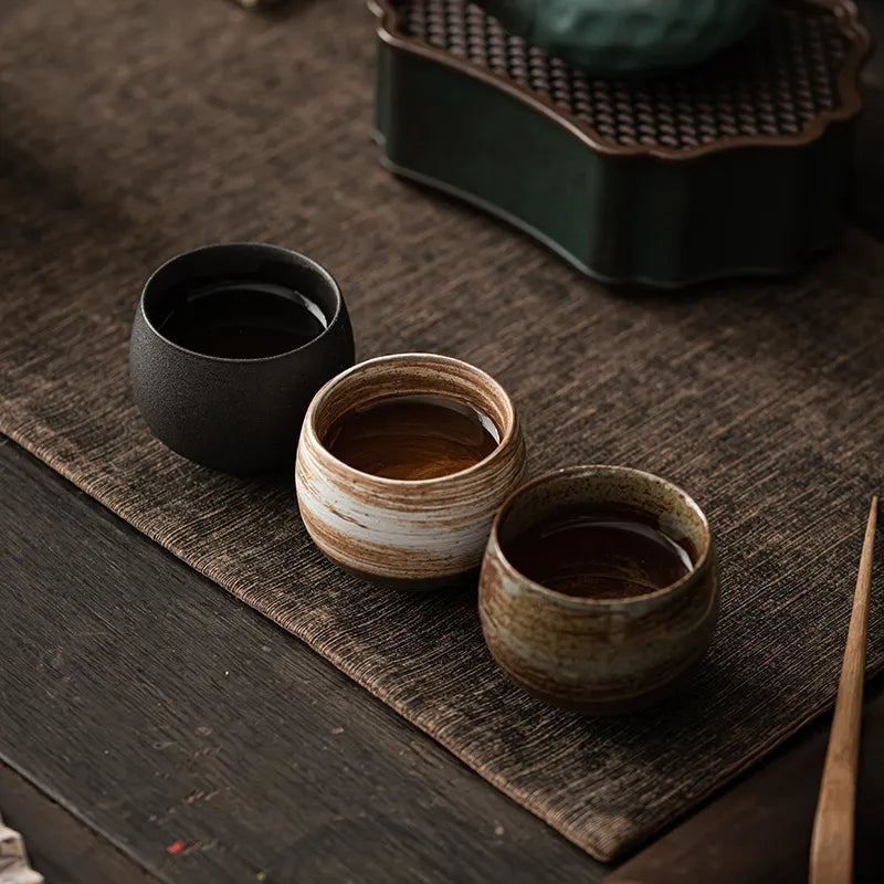 Three ceramic cups on a wooden surface with a teapot in the background