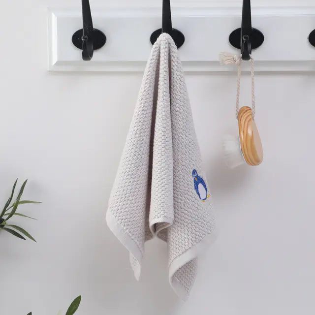 White textured towel with a penguin design hanging on a hook against a white wall.