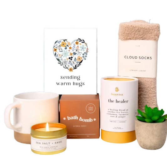 Collection of self-care items including a mug, candles, and bath products with a 'sending warm hugs' card.