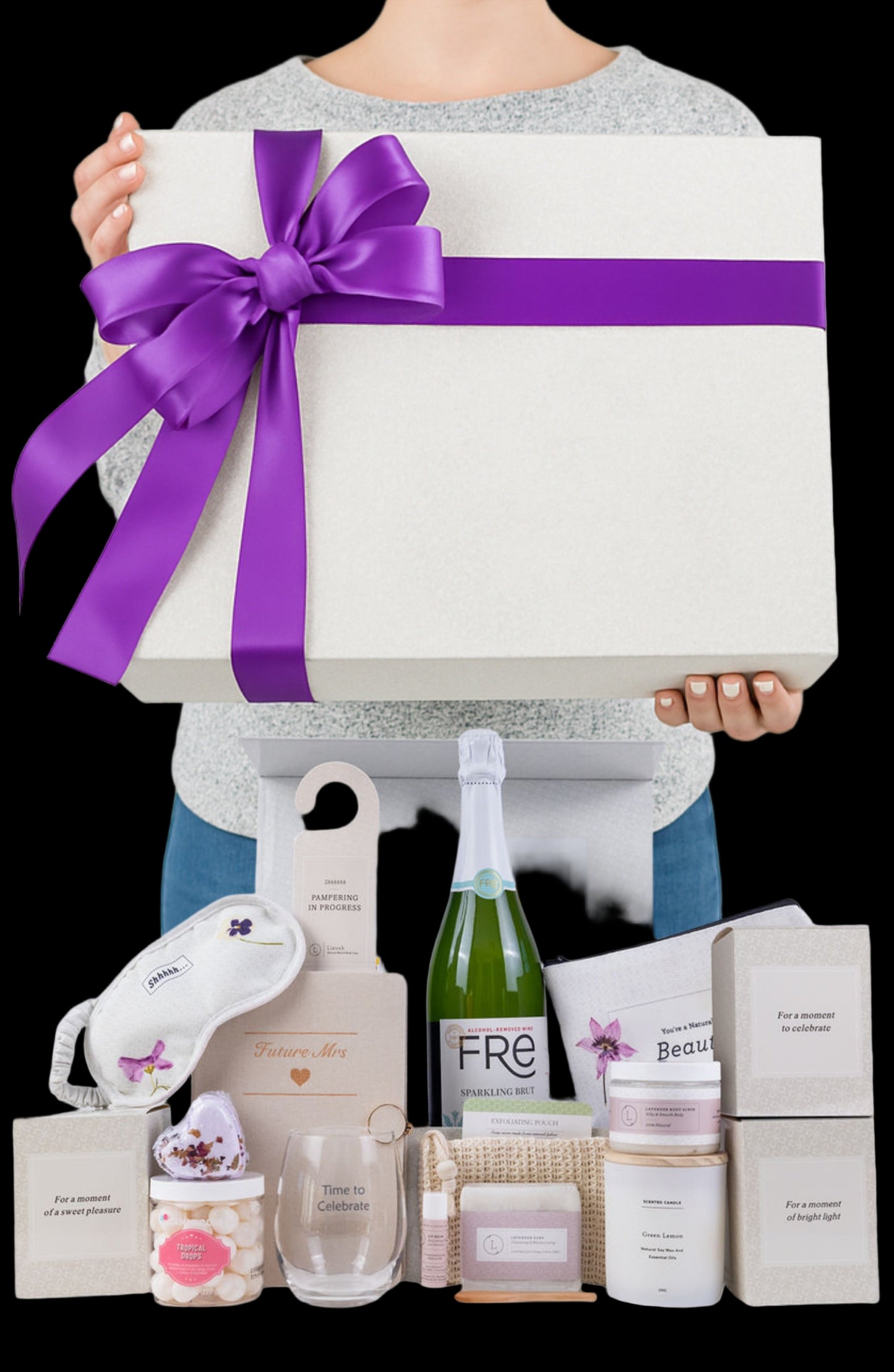Person holding a large gift box with a purple ribbon, surrounded by various beauty products on a white background.