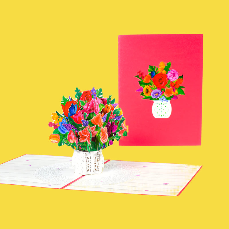 Colorful bouquet of flowers in a vase next to a matching floral-themed greeting card on a white background.