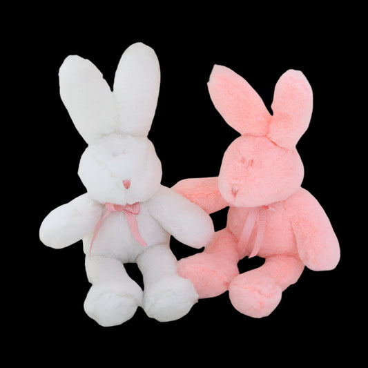 Two plush bunny toys, one white and one pink, sitting on a soft surface.