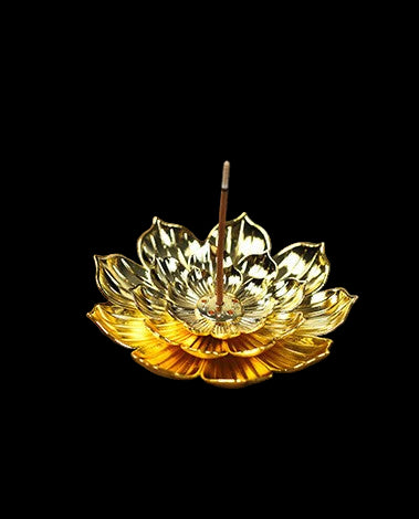 Gold lotus-shaped incense burner with a single incense stick on a wooden surface.