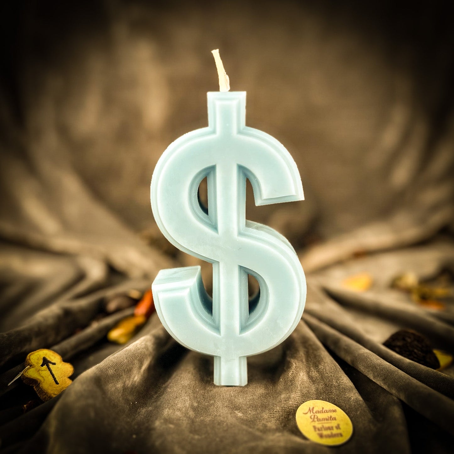 Candle shaped like a dollar sign on a textured fabric background
