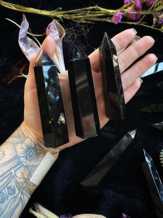 Hand holding black crystal sticks with a dark background and spider web decoration