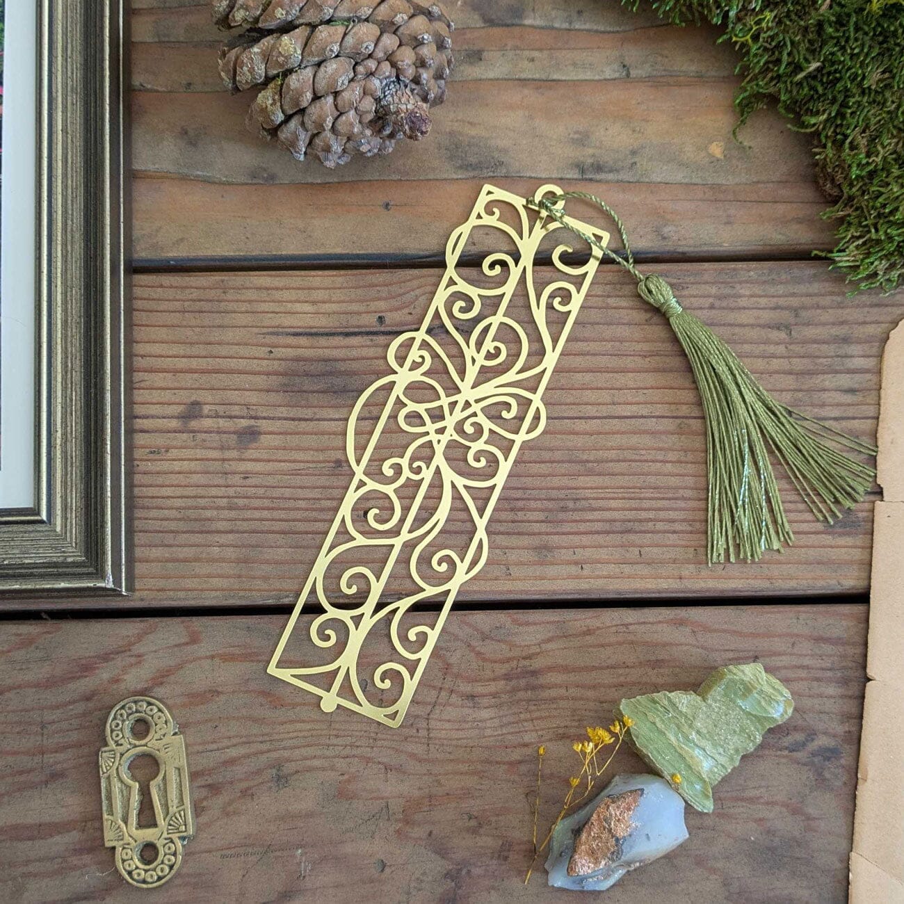 Decorative gold bookmark with tassel on a wooden surface with natural elements.