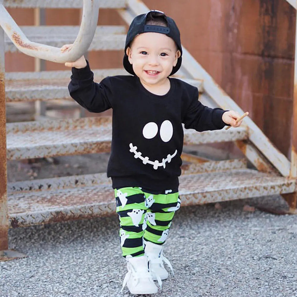 Child wearing a black shirt with a smiley face and green striped pants on a staircase.