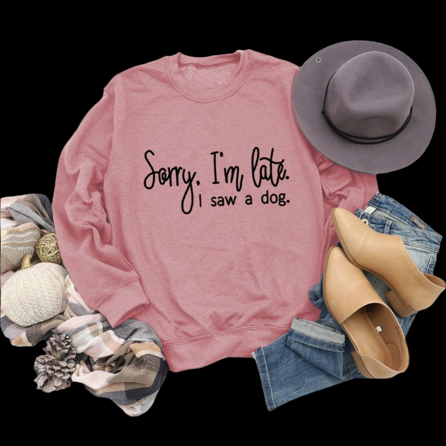 Pink sweatshirt with text, hat, shoes, and jeans on a wooden surface