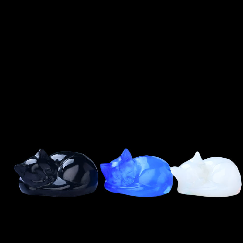 Three cat-shaped figurines in black, blue, and white on a light background with greenery.