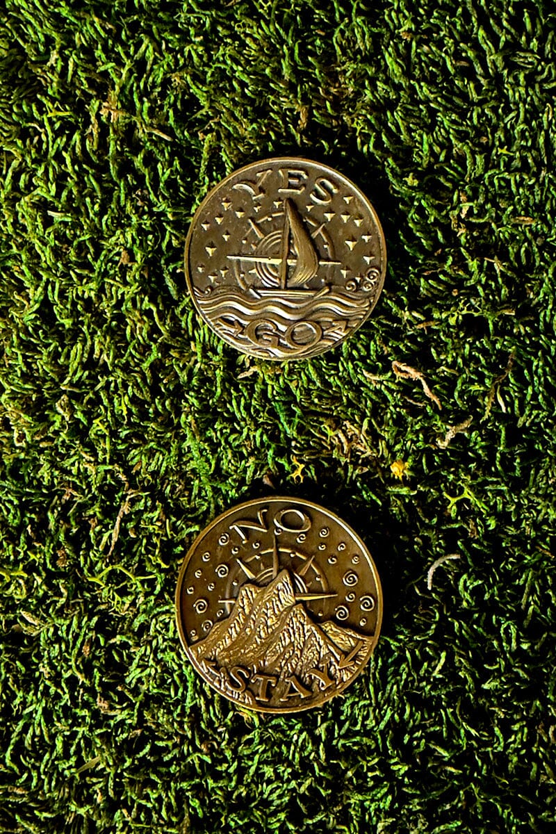 Two gold coins with ship and mountain designs on a green moss background