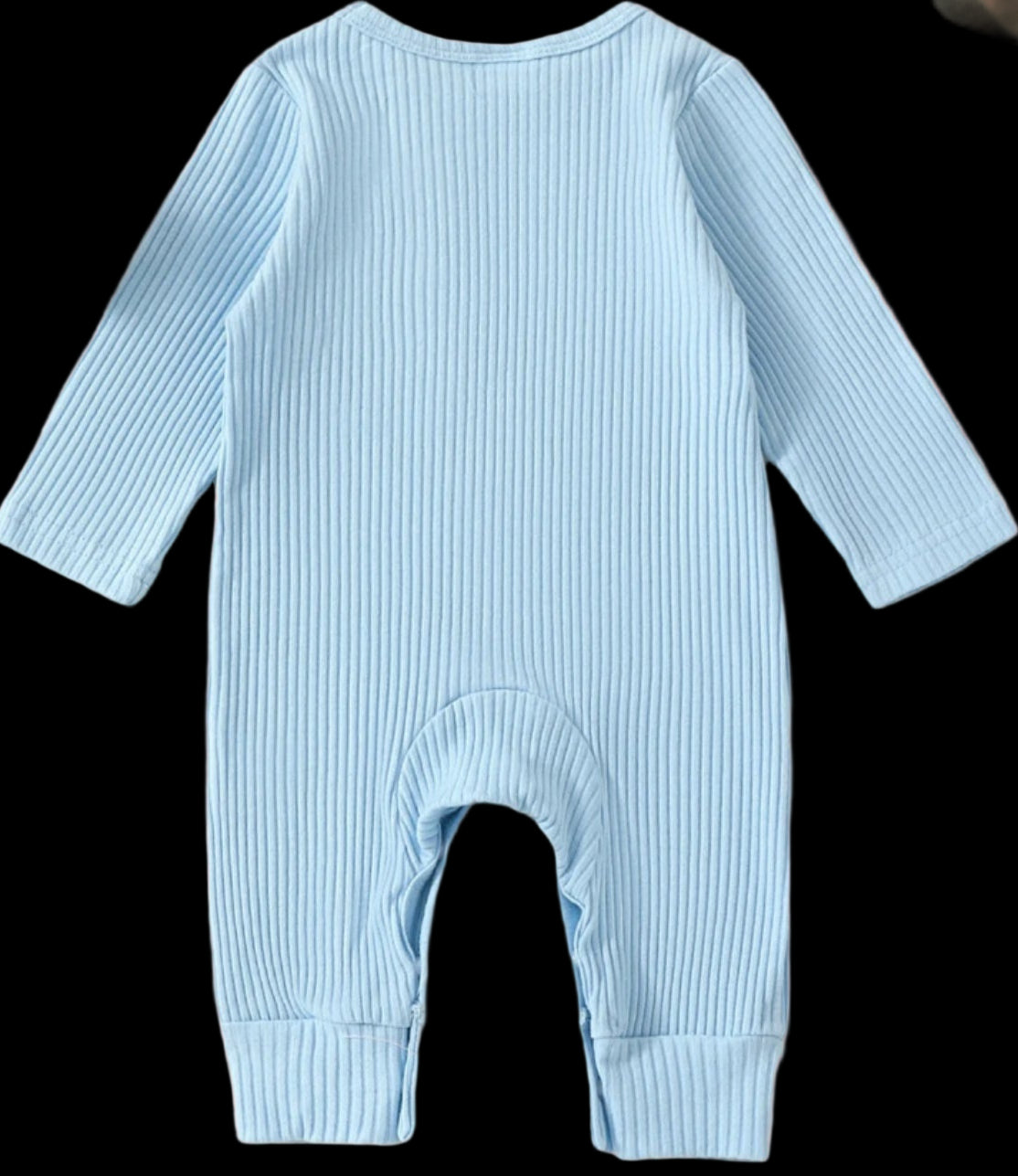 Light blue baby romper on a beige background with toys and plants.