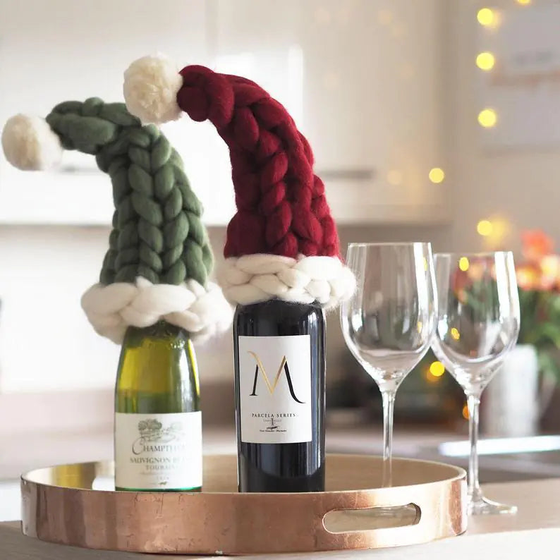Two bottles of wine with decorative hats on a tray with two glasses, blurred lights in the background