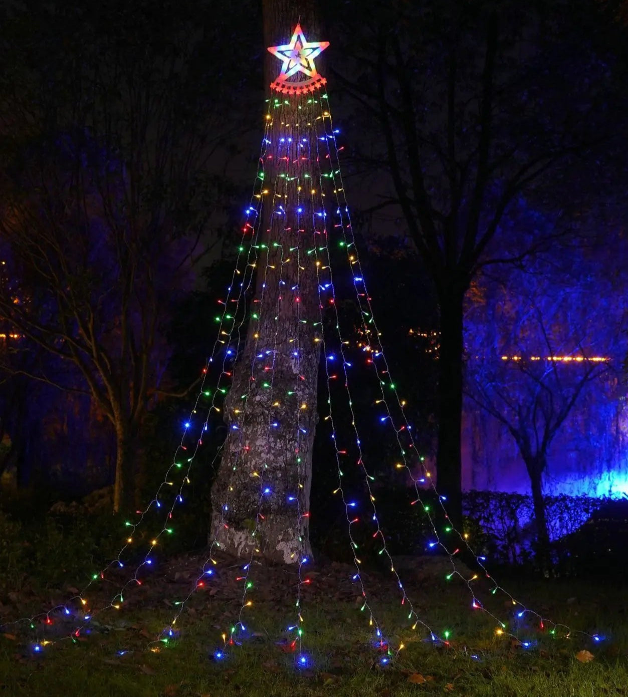 Decorative Christmas tree with colorful lights and a star on top in a dark outdoor setting.