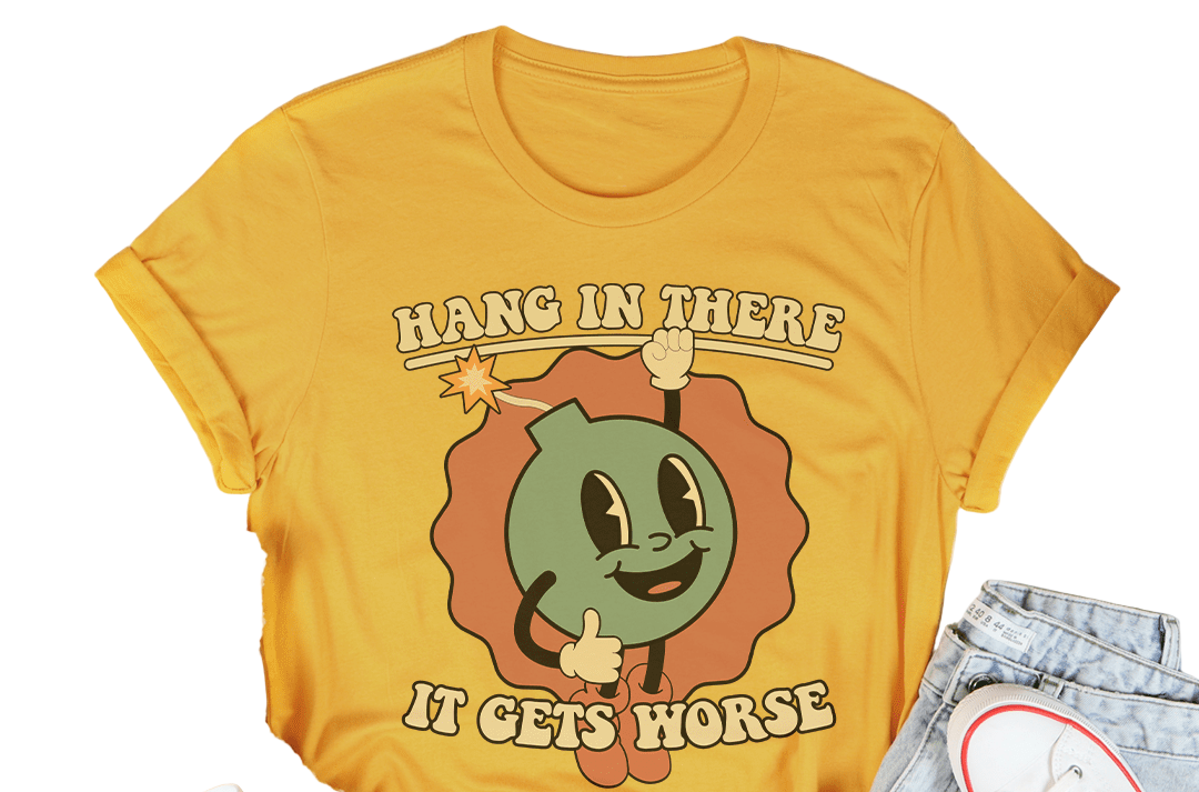 Yellow t-shirt with cartoon character and text 'Hang in there, it gets worse' on a white surface with casual items.