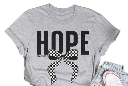 Gray t-shirt with 'HOPE' and a bow graphic, surrounded by casual items on a light wooden surface.