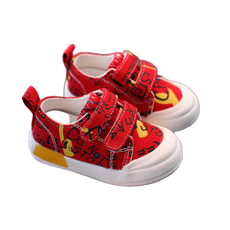 Red children's shoes with text held in a hand against a blurred background