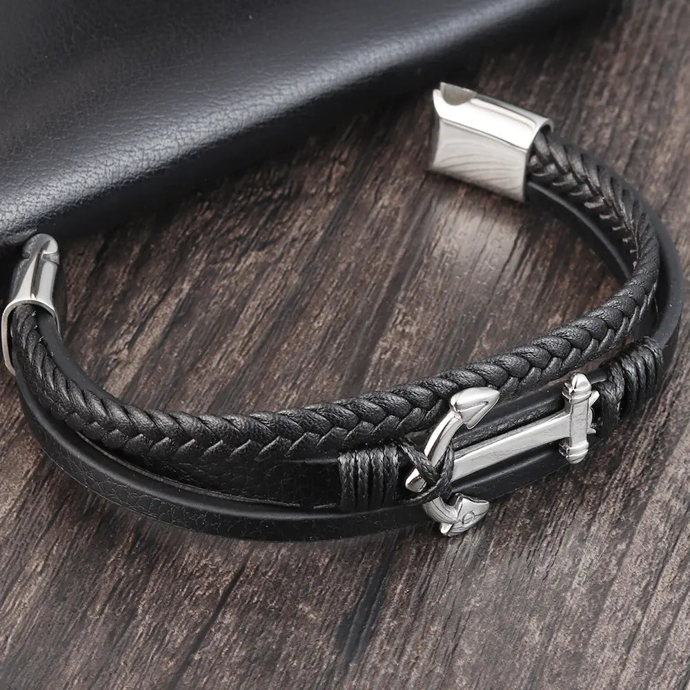 Black braided leather bracelet with silver anchor charm on a wooden surface