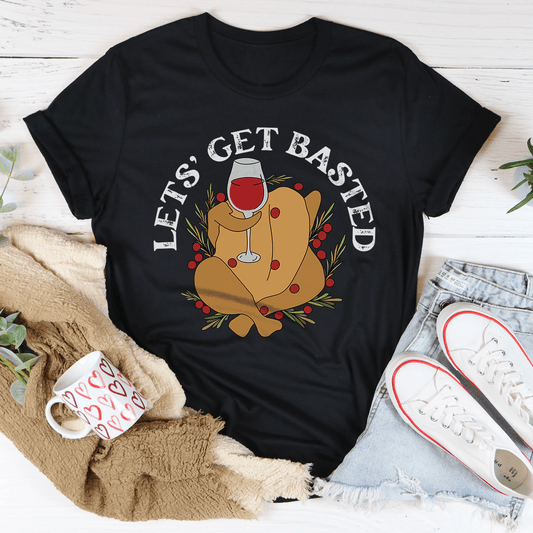 Black t-shirt with a graphic of a turkey and wine glass, text 'Let's Get Basted', on a white surface with casual items.