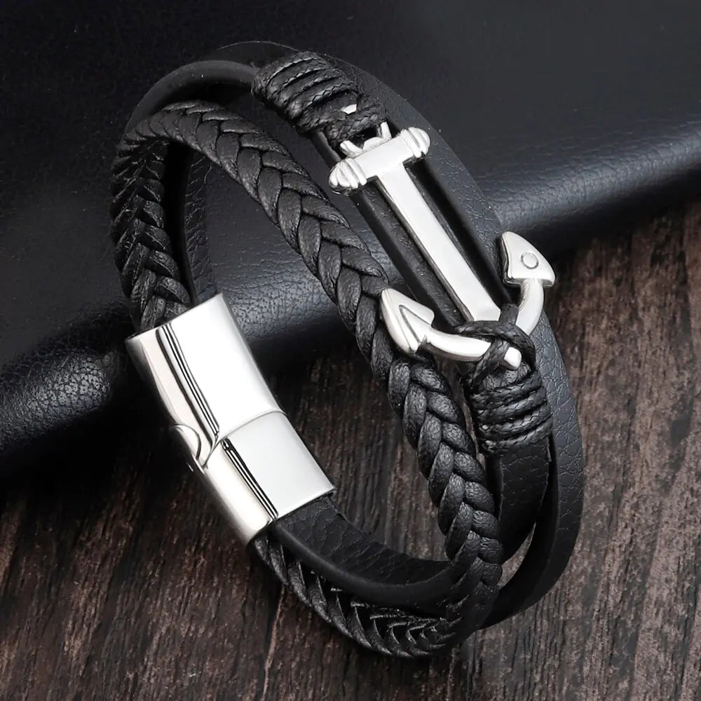 Black braided leather bracelet with silver anchor charm on a dark wooden surface