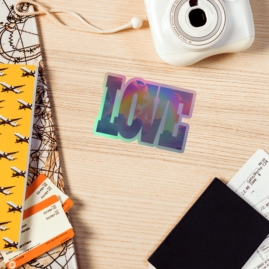 Colorful 'LOVE' sticker on a wooden surface with a camera and travel-themed items.