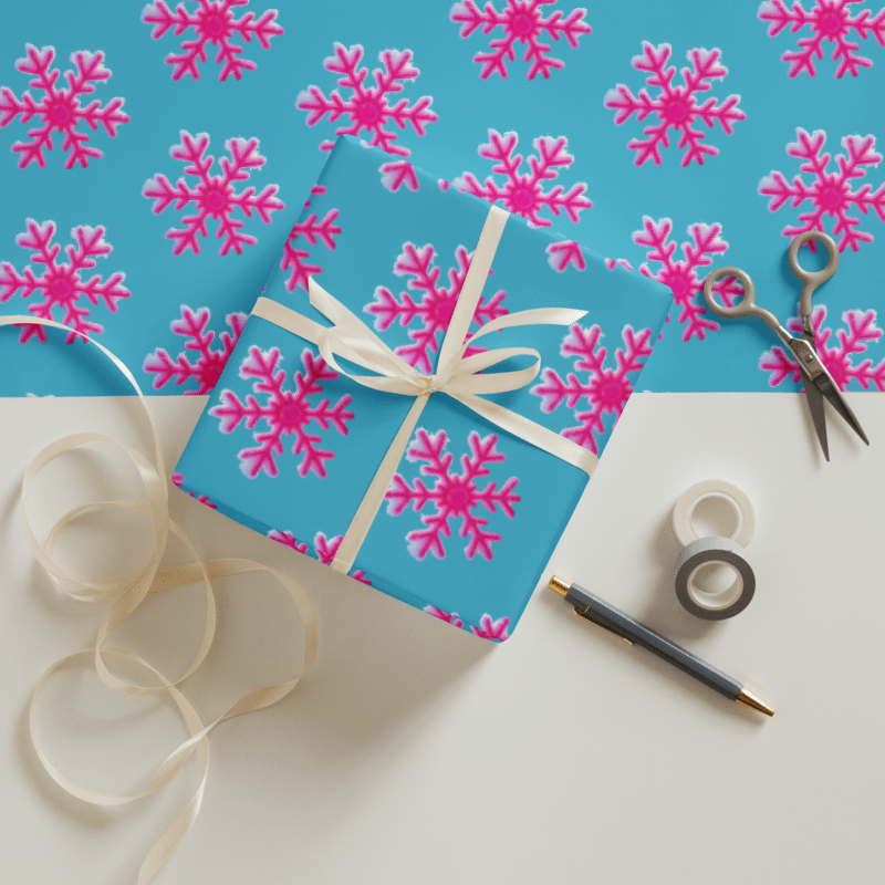Gift box with pink snowflake pattern on blue background, surrounded by ribbon, scissors, and tape.